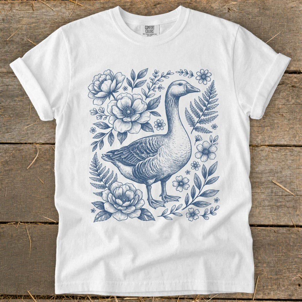 White t-shirt with blue line drawing of a goose surrounded by flowers and ferns.