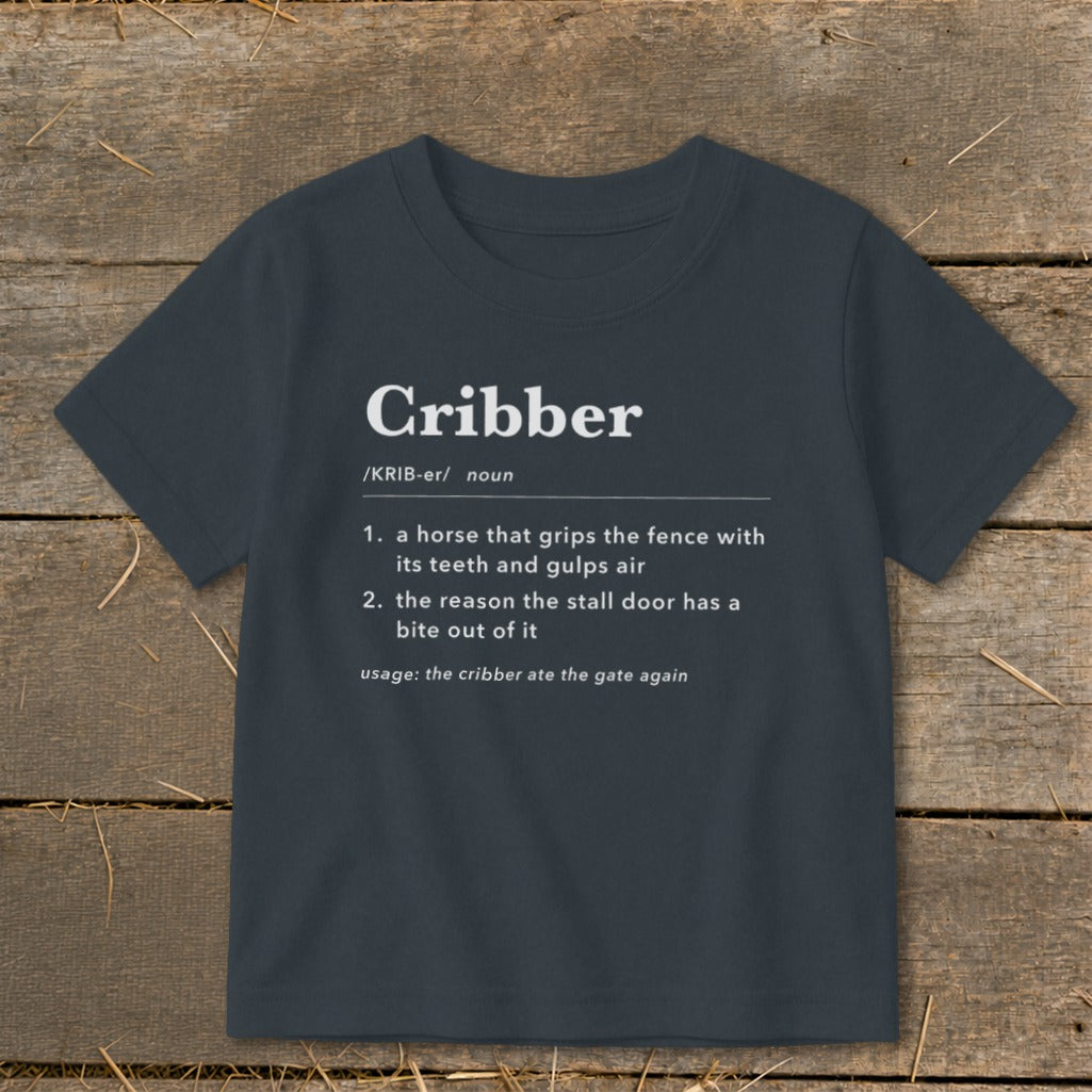 Dark grey t-shirt featuring dictionary-style text defining the word Cribber on a wooden background.