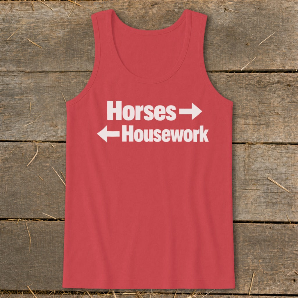 A red tank top with white text that reads Horses with a right arrow above Housework with a left arrow, laid flat on rustic wood.