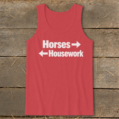 A red tank top with white text that reads Horses with a right arrow above Housework with a left arrow, laid flat on rustic wood.