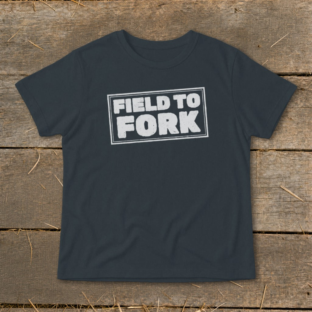 Dark gray crewneck t-shirt with the white distressed text "FIELD TO FORK" inside a rectangular border, laid flat on rustic wood.