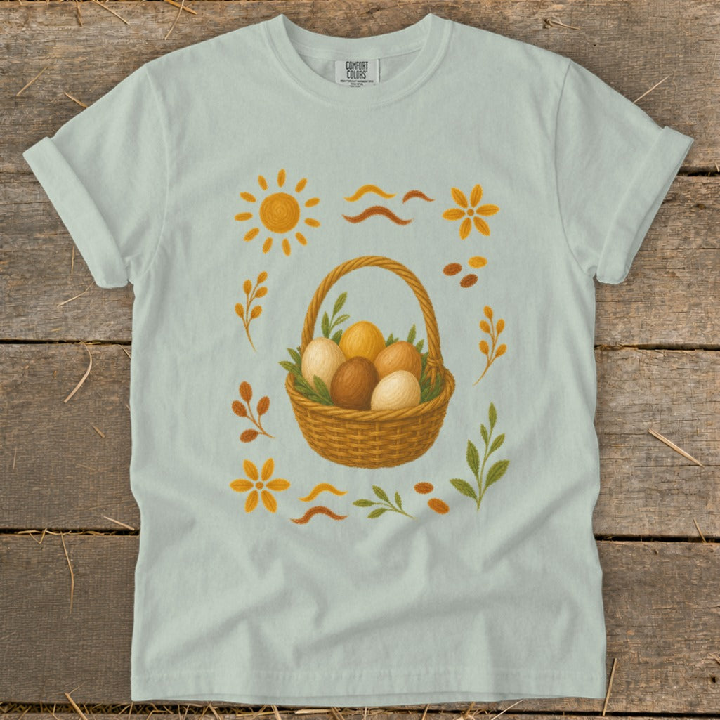Light blue t-shirt with a basket of eggs and Easter-themed embellishments.