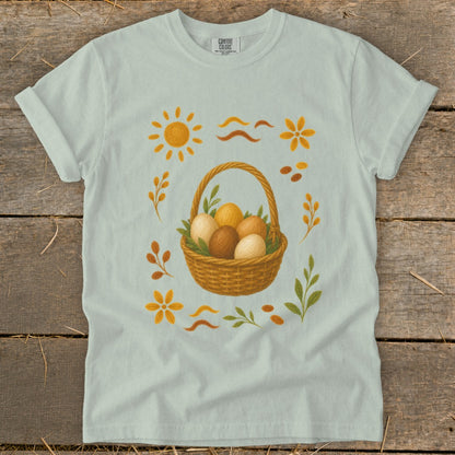Light blue t-shirt with a basket of eggs and Easter-themed embellishments.