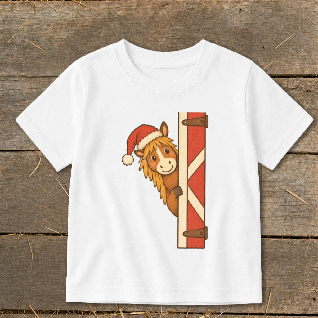 White t-shirt with cartoon horse wearing a Santa hat peeking from behind a red barn door.