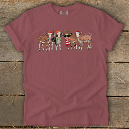 Five festive cows wearing Santa hats and Christmas lights, one with sunglasses.