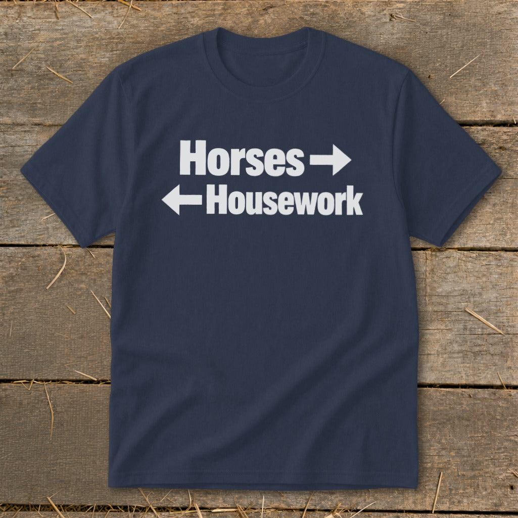 A dark blue t-shirt with white text that reads Horses with a right arrow and Housework with a left arrow.