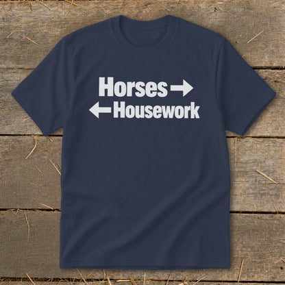 A dark blue t-shirt with white text that reads Horses with a right arrow and Housework with a left arrow.