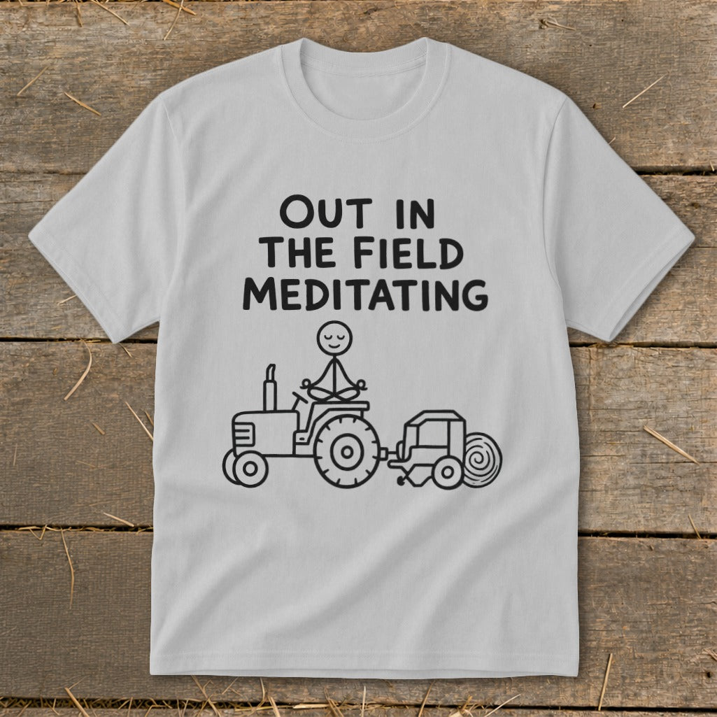 White t-shirt with "Out in the Field Meditating" text and stick figure on tractor.