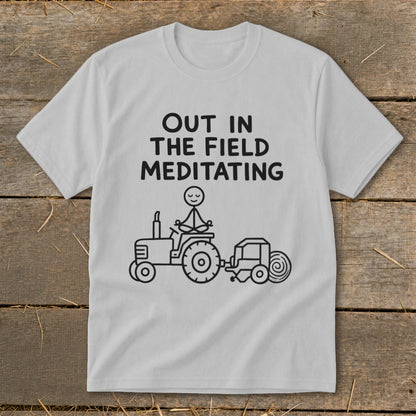 White t-shirt with "Out in the Field Meditating" text and stick figure on tractor.