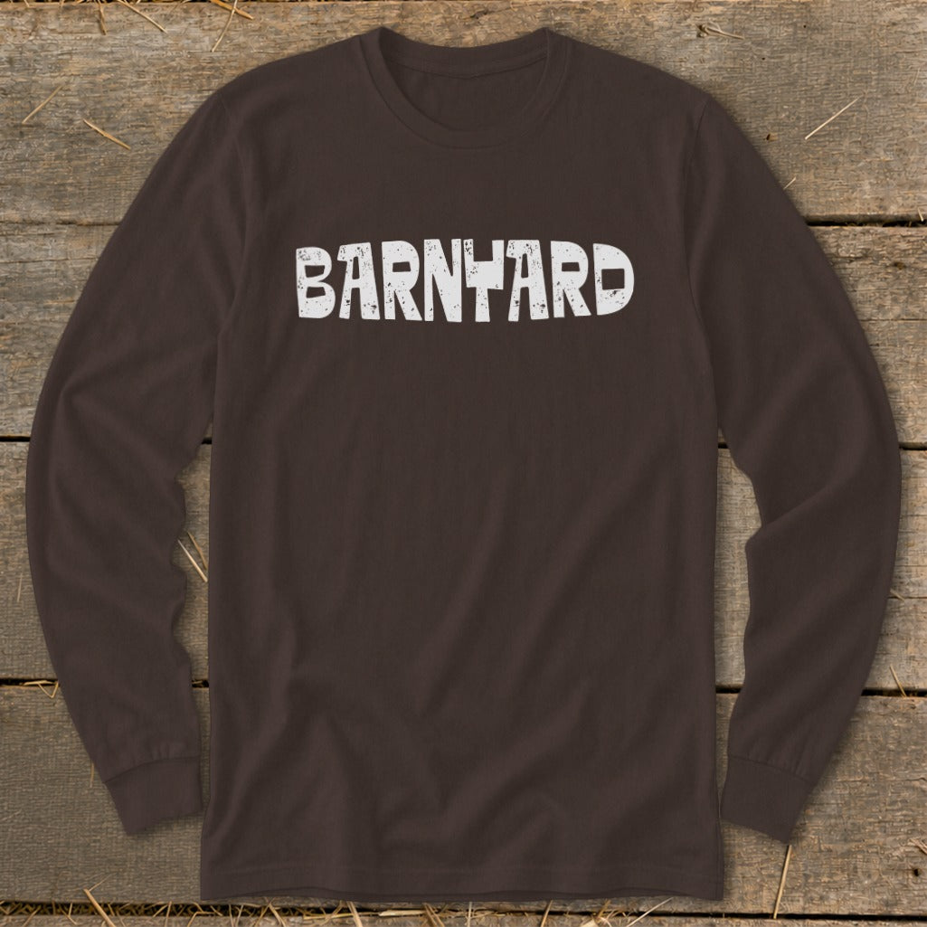 A dark brown long-sleeve t-shirt with the distressed white text "BARNYARD" centered on the chest, laid flat on a rustic wooden background.