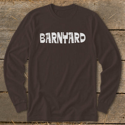 A dark brown long-sleeve t-shirt with the distressed white text "BARNYARD" centered on the chest, laid flat on a rustic wooden background.
