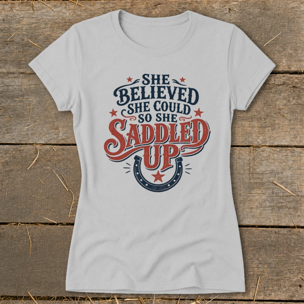 Light grey t-shirt with text "She Believed She Could So She Saddled Up" and horseshoe graphic.