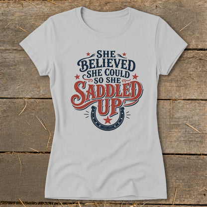 Light grey t-shirt with text "She Believed She Could So She Saddled Up" and horseshoe graphic.