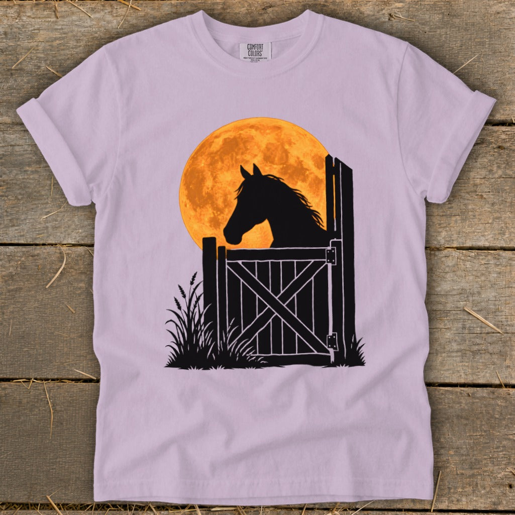 Light purple t-shirt featuring a graphic of a horse silhouette looking over a stable door against a large orange moon.