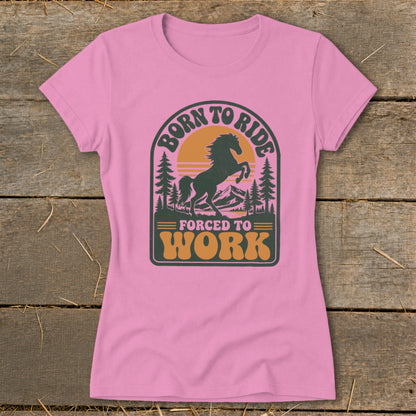 Pink t-shirt with graphic of a horse, mountains, trees, and text "Born to Ride Forced to Work".