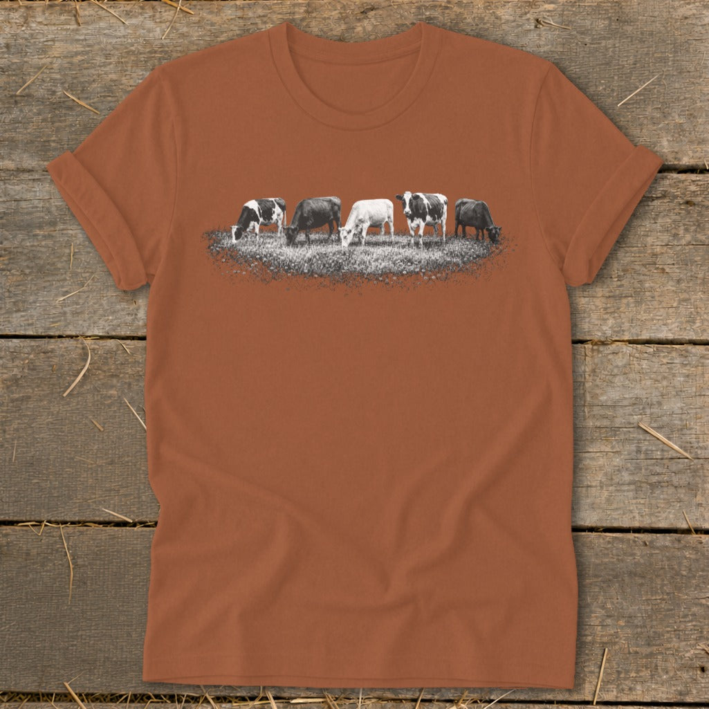 Five cows graze in a field with a distressed graphic on a terracotta t-shirt.