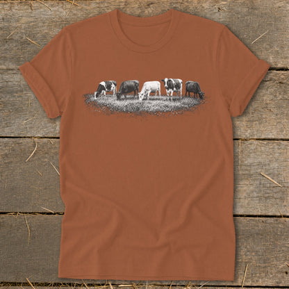 Five cows graze in a field with a distressed graphic on a terracotta t-shirt.