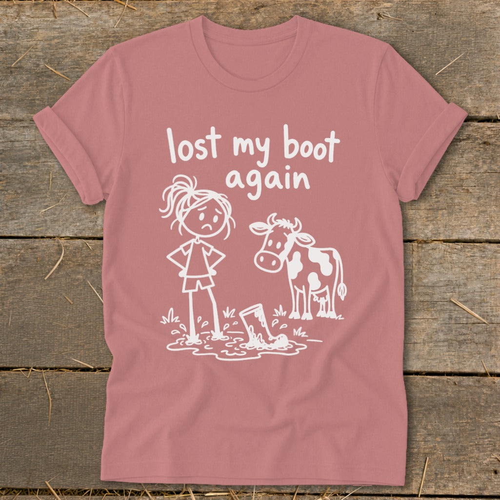 Dusty rose t-shirt featuring a white graphic of a sad girl and a cow looking at a boot in a mud puddle, with the text "lost my boot again".