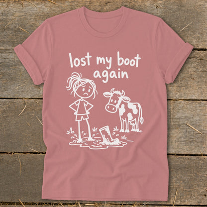 Dusty rose t-shirt featuring a white graphic of a sad girl and a cow looking at a boot in a mud puddle, with the text "lost my boot again".