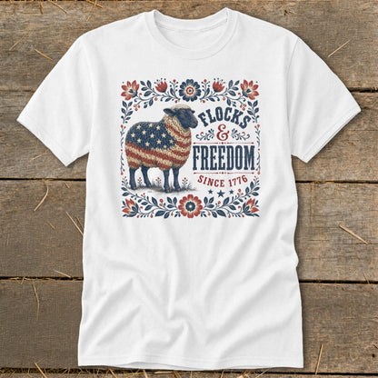 White t-shirt with a sheep graphic in American flag colors and text "FLOCKS & FREEDOM SINCE 1776."