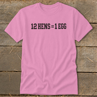 Pink t-shirt with black block lettering on the chest reading 12 HENS = 1 EGG, laid flat on wooden planks.