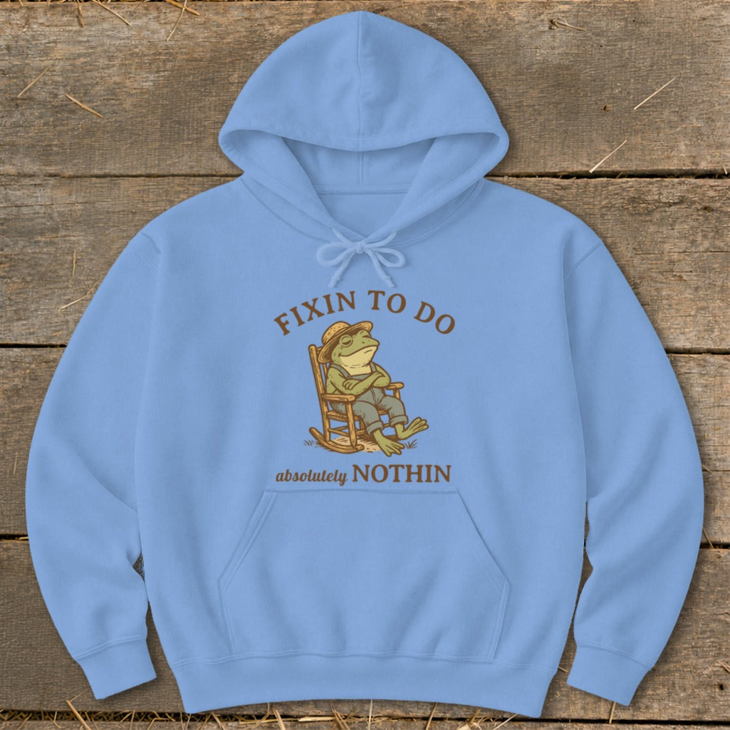 Light blue hoodie with cartoon frog relaxing in rocking chair, text "FIXIN TO DO absolutely NOTHIN".