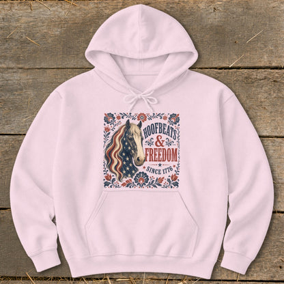 Pink hoodie with a horse graphic featuring American flag colors and text "Hoofbeats & Freedom Since 1776".