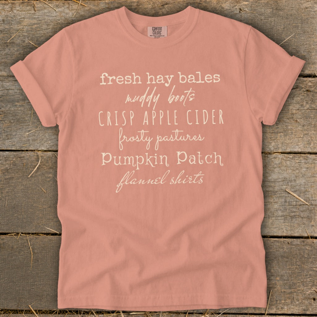 Peach t-shirt with white text listing "fresh hay bales, muddy boots, crisp apple cider, frosty pastures, pumpkin patch, flannel shirts."
