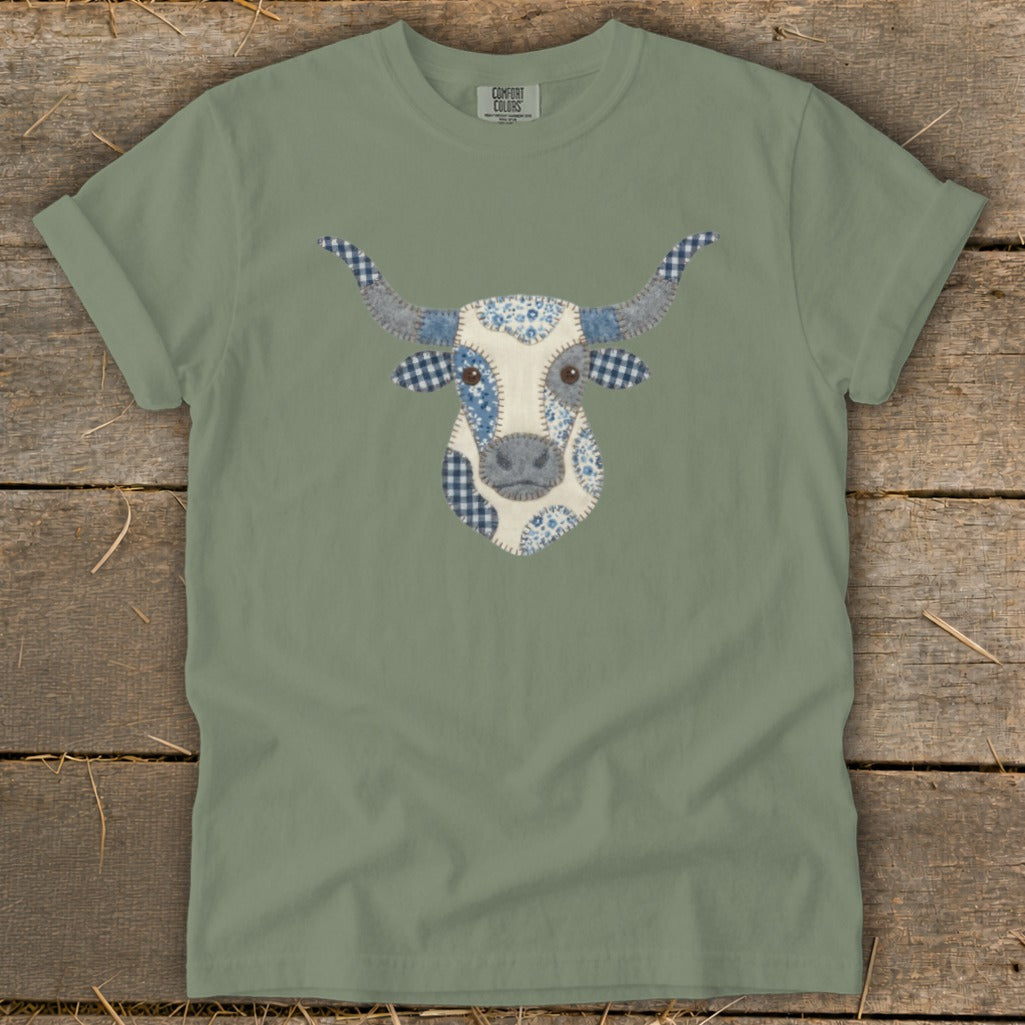 Green t-shirt with a patchwork cow face graphic featuring blue and white patterns.