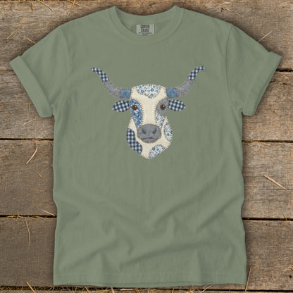 Green t-shirt with a patchwork cow face graphic featuring blue and white patterns.