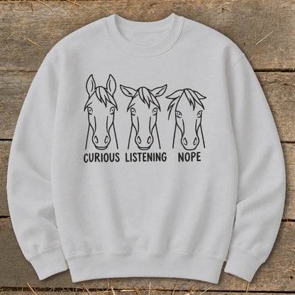 Light gray crewneck sweatshirt featuring a graphic of three horse heads with the text "CURIOUS," "LISTENING," and "NOPE."