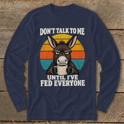 Dark blue long-sleeve t-shirt featuring a grumpy donkey holding a coffee mug against a retro sunset.