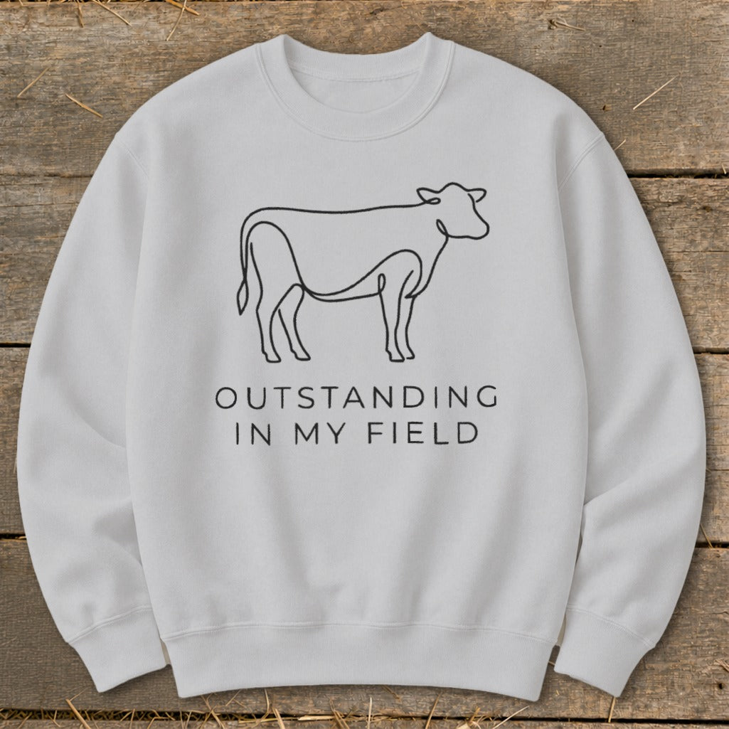 Light gray sweatshirt with black line drawing of a cow and text "OUTSTANDING IN MY FIELD".