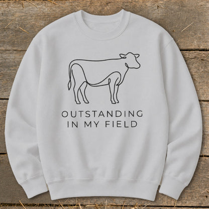 Light gray sweatshirt with black line drawing of a cow and text "OUTSTANDING IN MY FIELD".