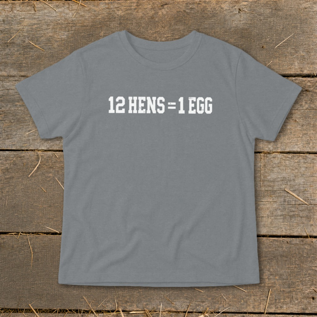 A gray crewneck t-shirt with the white distressed text 12 HENS equals 1 EGG on the chest, laid flat on a rustic wooden background.