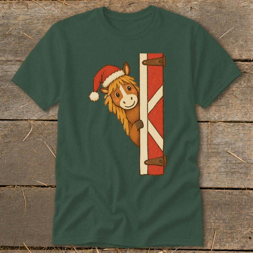 Horse in a Santa hat peeking around a barn door on a green t-shirt.