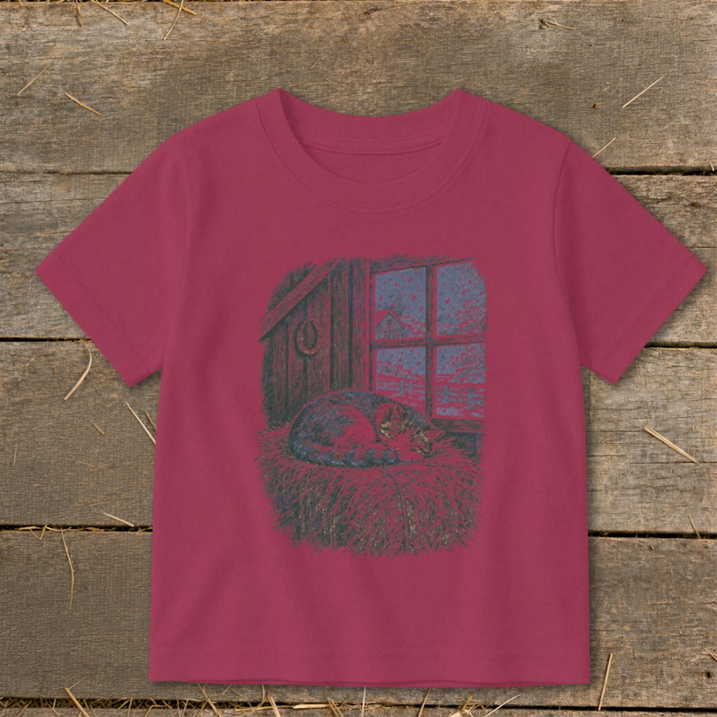 T-shirt graphic of a tabby cat sleeping in straw by a window with a barn scene.