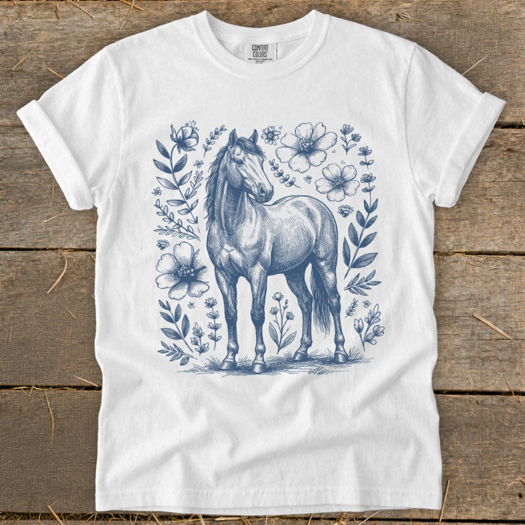 White t-shirt with blue sketch of a horse surrounded by flowers and leaves.