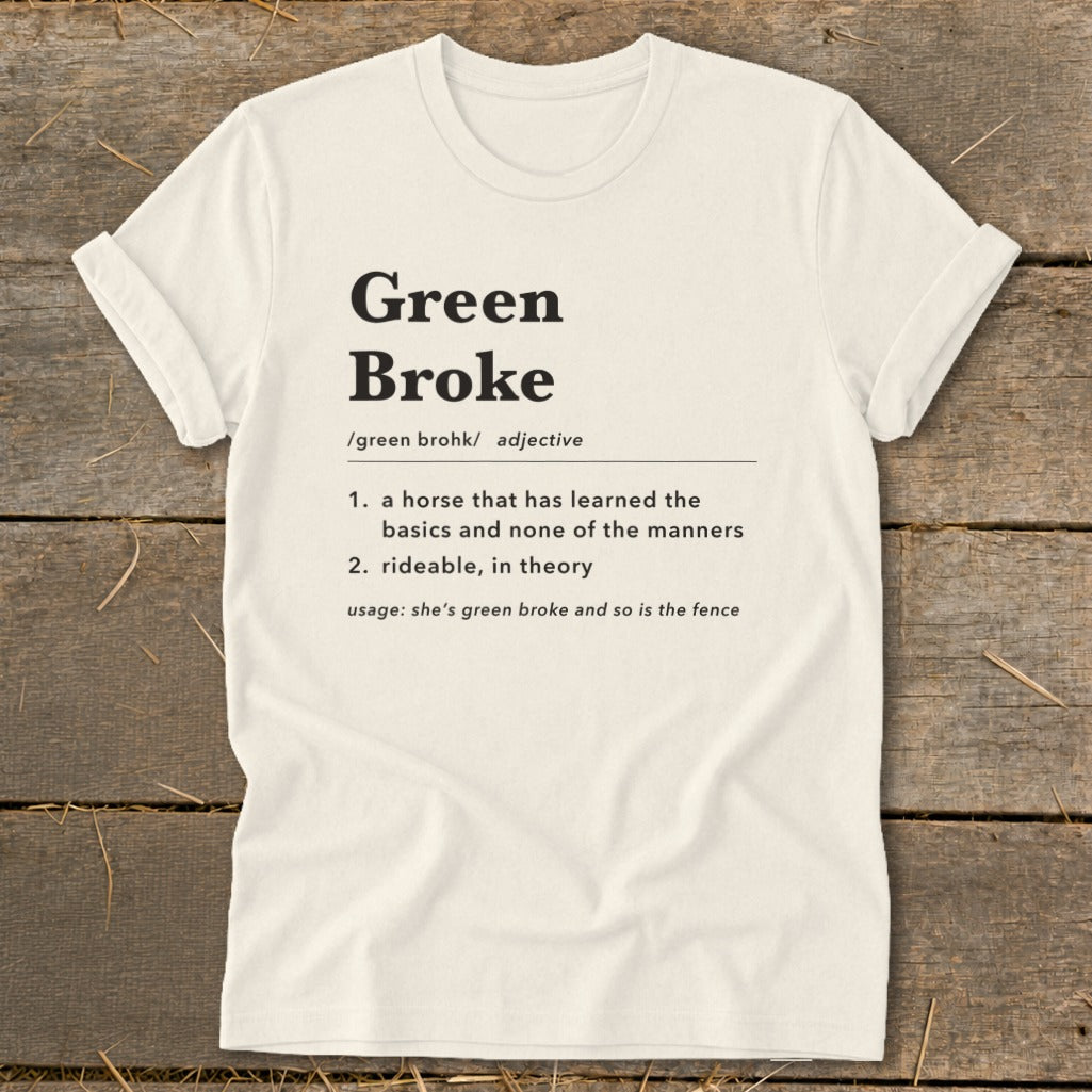 Off-white t-shirt with black dictionary-style text defining the term green broke centered on the chest, laid flat on a wooden surface.