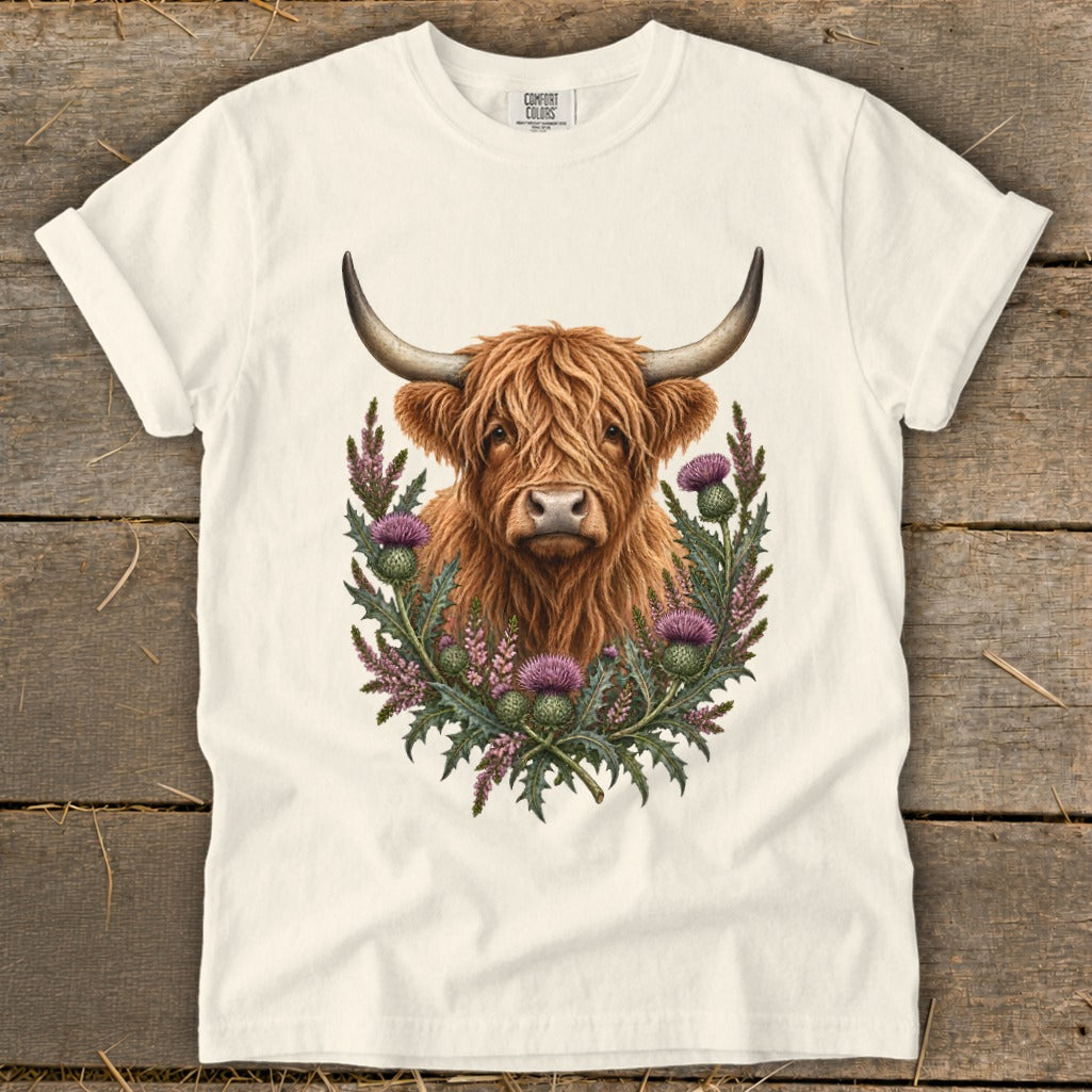 Highland cow portrait surrounded by thistles on a cream t-shirt.