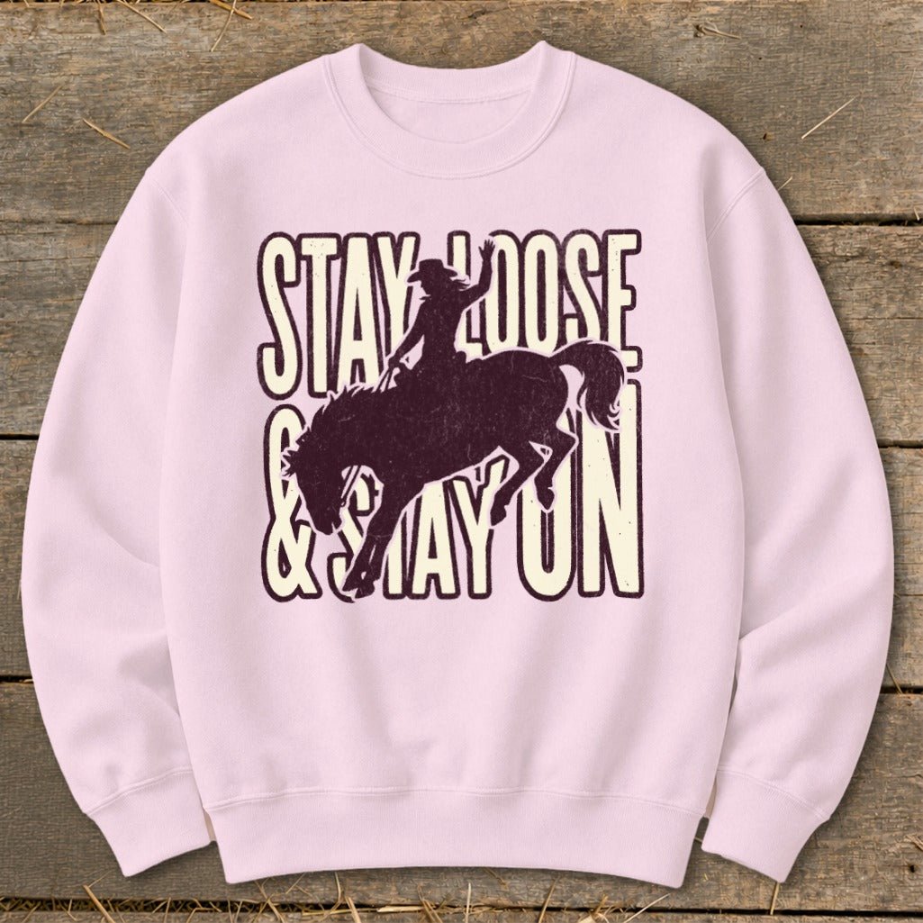 Pink sweatshirt with distressed "STAY LOOSE & STAY ON" text and cowboy silhouette on horse.