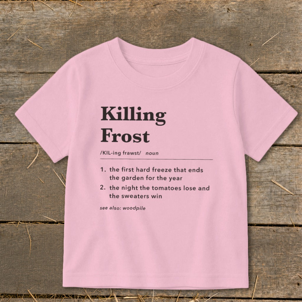 A light pink t-shirt with black dictionary-style text defining Killing Frost displayed flat on a wooden background.
