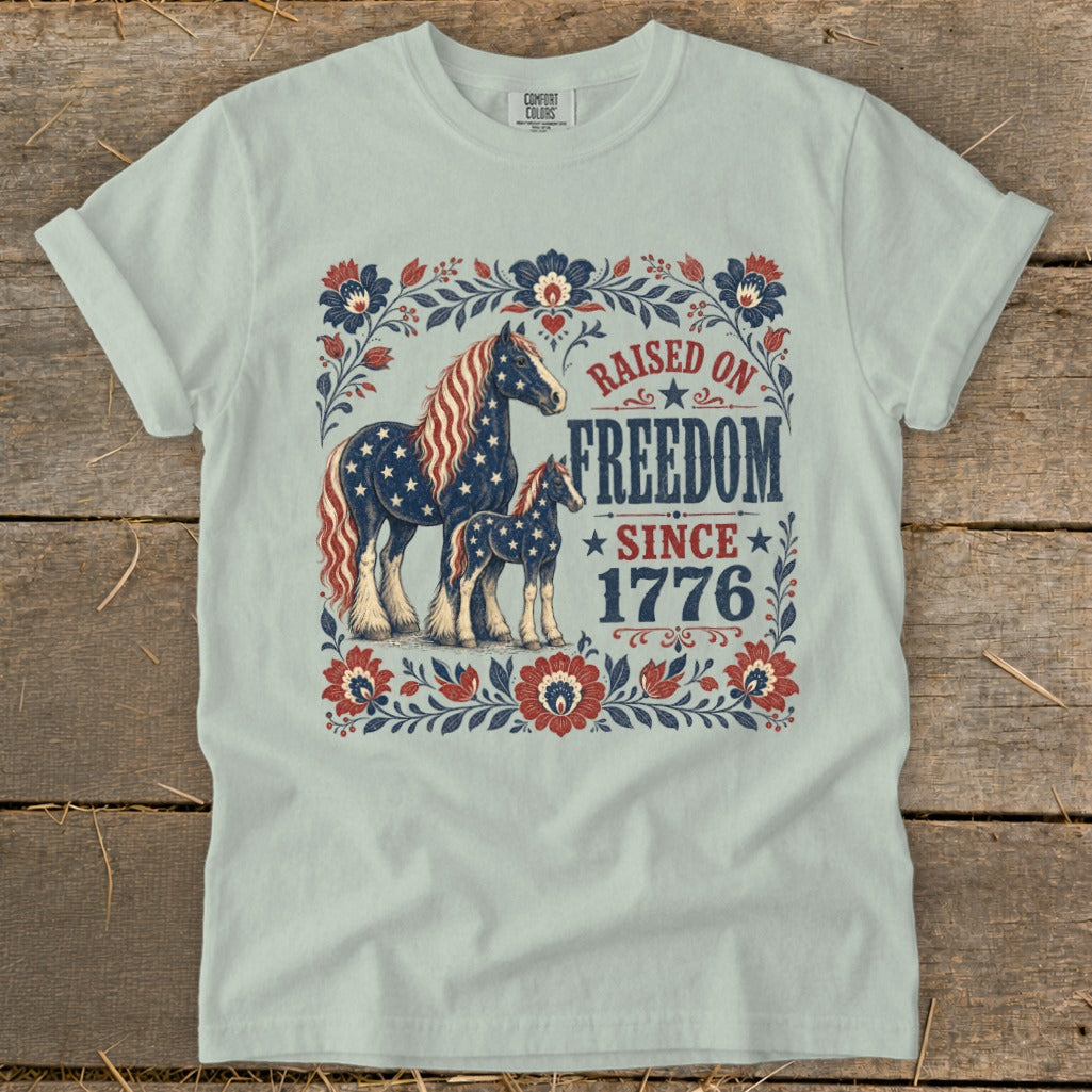 Light blue t-shirt with horses and "Raised on Freedom Since 1776" text.