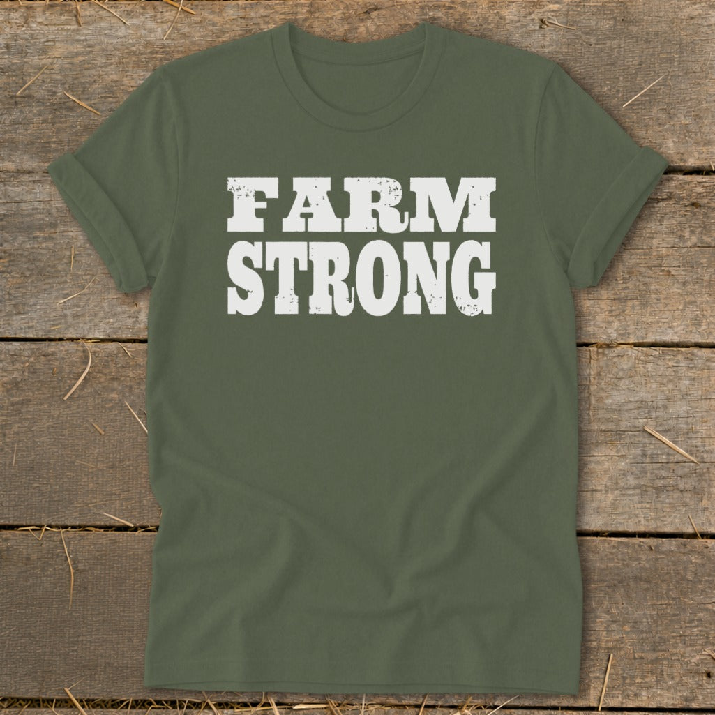 An olive green crewneck t-shirt with distressed white text reading FARM STRONG, displayed flat on a wooden surface.