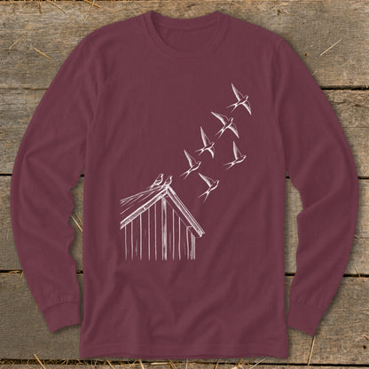Maroon long-sleeve t-shirt featuring a white line drawing of birds flying from a rustic wooden shed.