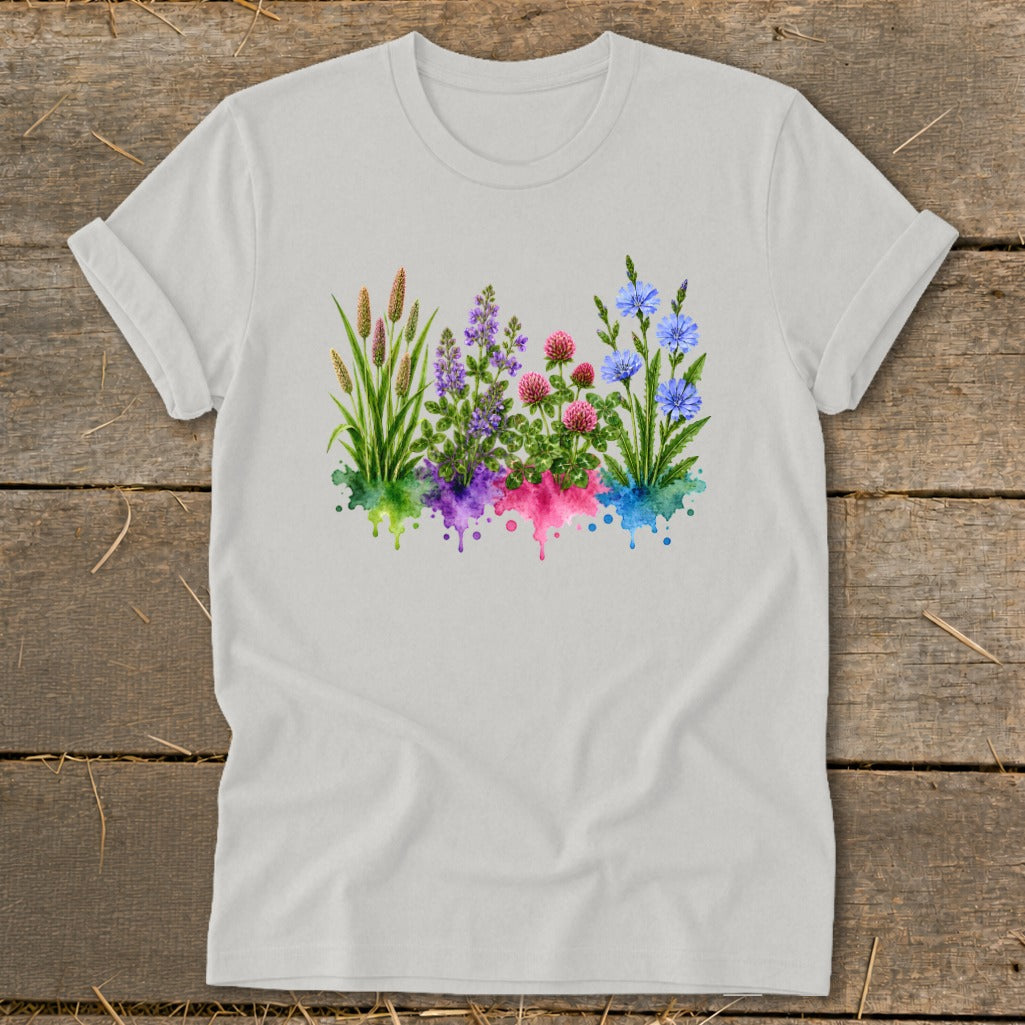 A light gray crewneck t-shirt with rolled sleeves features a colorful watercolor botanical graphic on a wooden surface.
