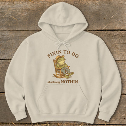 Cream hoodie with graphic of a frog in a rocking chair saying "Fixin to do absolutely nothin".