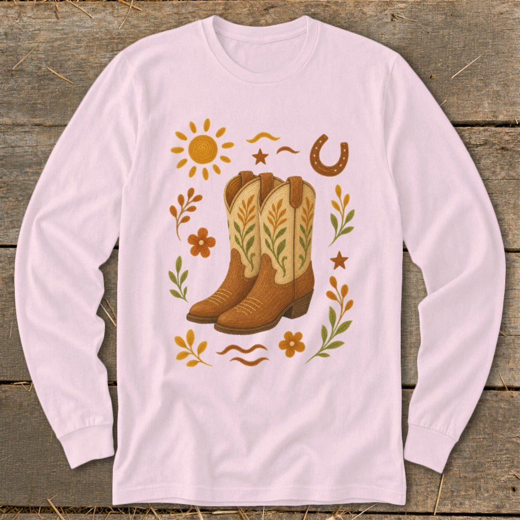 Cowboy boots surrounded by sun, horseshoe, flowers, and leaves on a pink long-sleeve shirt.