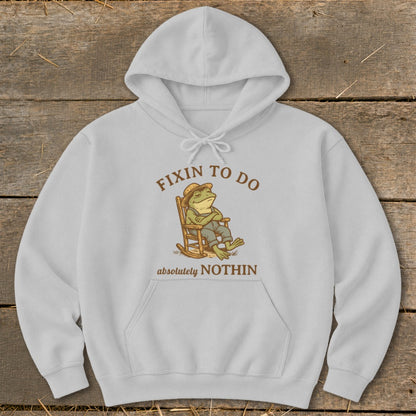 Light grey hoodie with "Fixin to do absolutely nothin" text and frog on rocking chair graphic.