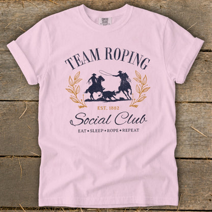 Pink t-shirt with "Team Roping Social Club" graphic and "Eat Sleep Rope Repeat" text.